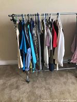 Photo showing multiple women's large size clothing items hanging on a metal clothing rack with wheels on a carpeted floor.