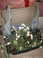 Plastic storage bin filled with faux flowers and two composite wood birds