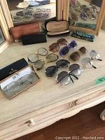All ten pairs of women's eyeglasses and sunglasses laid out on a surface with six eyeglasses cases behind them.
