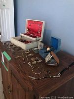 Wide shot showing jewelry box open with red interior, assortment of jewelry on wood surface