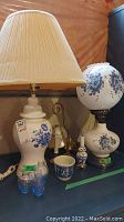 Image showing two ceramic table lamps, one with fabric shade and one with globe-shaped glass shade adorned with blue floral designs. Also visible are miniature blue glass vases and ceramic decorative items in front.