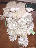 Top view of assorted vintage table linens and doilies spread on a wooden floor, showing various lace and crochet designs.