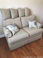 Front view of beige Ethan Allen upholstered love seat with six cushions arranged on and around it