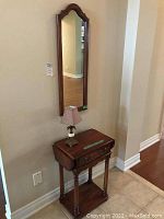 Wide view showing mirror hanging above the drop leaf wooden table with a drawer, lamp on top, positioned against a wall.