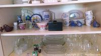 Upper shelf with various cups, mugs, teapot, bowl, small plates and decorative bird figurines.