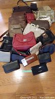Lot of assorted purses, bags, and wallets spread out on floor showing size and style variety