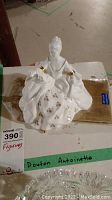 White porcelain Royal Doulton figurine named Antoinette with gold accents, photographed on a white surface with identifying labels visible.