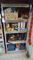 Full view of metal shelving unit loaded with various loose hardware parts and tools stored on shelves.