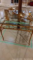 Front angle view of gold-tone metal side table with glass top, with decorative items present but not included