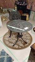 Photo shows round cast metal table with glass top and ornate cut-out pattern casting shadow on floor, part of basement setting