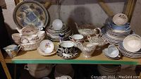 Full view of multiple sets of plates, cream and sugar pots, teapots, and teacups arranged on shelf