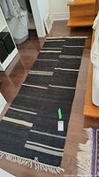 View of black runner mat on hardwood floor with linear stripe pattern and fringed ends