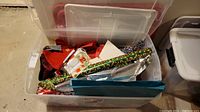 Clear plastic bin filled with various rolls of Christmas wrapping paper, gift bags, and other wrapping supplies.