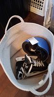 Top view inside white fabric basket showing blue helmet and pair of black and white children's ice skates.