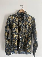 Front view of dark dress shirt featuring gold floral pattern hanging on wooden hanger.