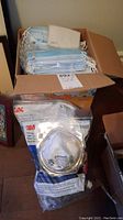 Box containing stacked blue surgical face masks and several sealed 3M particulate respirator masks.