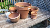 Six terracotta planters displayed on wooden table, showing sizes and shapes
