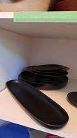 Black ceramic plates and an elongated serving tray stacked in a cupboard corner.
