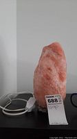 Front view of pink Himalayan salt lamp with attached white power cord and inline switch on black surface.