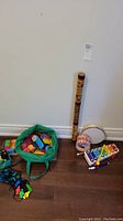 Wide shot showing green bag of large colorful building blocks and assortment of musical instruments (didgeridoo, tambourine, drums, xylophone) on floor