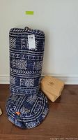 Two patterned yoga cushions in indigo with white designs, one cylindrical and one circular, standing against the wall with two cork yoga blocks beside them.
