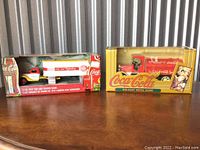 Two original boxed 1/43 1937 Coca-Cola cab and trailer die-cast metal banks side by side, showing front of packaging with logos and design.