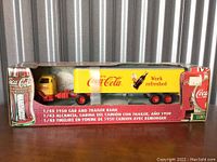 Front and partial side view of the Coca-Cola 1950 cab and trailer bank in original packaging with visible brand and scale details.