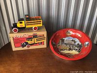 Photo of 1931 Hawkeye Coca-Cola Beverage Truck Bank on box next to a large round Coca-Cola decorative tray