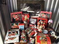 Photo showing a variety of Coca-Cola Christmas collectibles including tins, puzzles, figurines, and other decorations arranged on table.