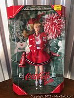 Full front view of Barbie doll in original box with red and white cheerleading outfit and Coca-Cola branding visible.