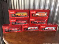 Eight boxed 1:87 scale Ford C Tractor beverage trailers with Coca-Cola and Fanta branding displayed on table