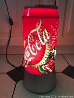 Front and side view of the illuminated Coca-Cola can shaped lamp with silver base on tile floor.