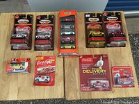 Overview of ten Coca-Cola branded Matchbox collectible vehicles in original sealed packaging displayed on wooden table.