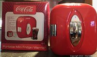 Photo of the product next to its original box showing the red portable mini fridge/warmer and product branding.