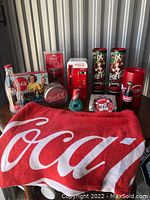 Full display of Coca-Cola variety lot including bottles, tins, vending machine replica, towel, pencil sharpener, and decorative containers