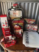 Full lot grouping of Coca-Cola vintage collectible items arranged on a small round table with metal siding background