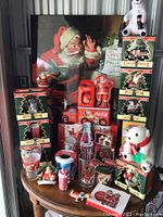 Full view of Coca-Cola Christmas collectibles on display table including figurines, glasses, plush, and signage.