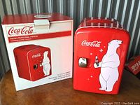 Photo of the red Coca-Cola retro personal fridge with polar bear design and its packaging box, showing front view with latch door closed.