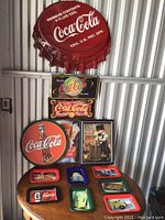 Full display of all Coca-Cola metal signs and trays arranged on wall and table showing variety of vintage advertising designs.