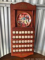 Front view of the wooden Coca-Cola calendar rack holding a single January collector plate in display, with movable number blocks arranged below.