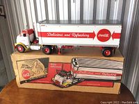 Photo showing Coca-Cola branded 1/25 scale tractor trailer model on top of original box with vintage Coca-Cola graphics and slogan 'Delicious and Refreshing'.