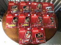 Full lot overview showing 10 unopened Coca-Cola die-cast cars with collectible tins on tabletop, including duplicates of numbers 5 and 6.