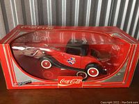 Front side view of the Ford Roadster die-cast model inside its original Coca-Cola branded box, showing car details and packaging condition.