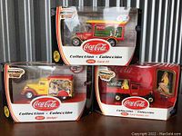 Four boxed Matchbox Coca-Cola collectible vehicles, shown in original packaging with clear windows, showcasing each die-cast vehicle with Coca-Cola advertising motifs.