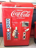 Front view of red Coca-Cola bottle vending machine with branding, coin slot, bottle opener, and bottle cap dispenser.