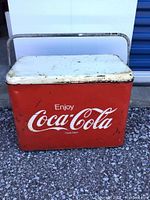 Front view showing red body with white Coca-Cola logo and white lid with rust and scratches.