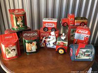 View of entire collection showing multiple Coca-Cola metal tins and two toy vehicles with moving parts.