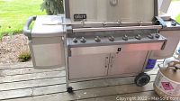 Front view of grill showing six control knobs, Weber logo on lid, rotisserie rod mounted across front