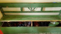 Front view of green storage bench with hinged lid open and contents visible