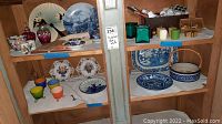 Two wooden shelves displaying various blue and white china plates, bowls, candle holders, and candles as described by seller.